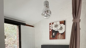 Ein Schlafzimmer mit Bett, Nachttisch, Wandleuchte und Fenster mit Blick auf Bäume.