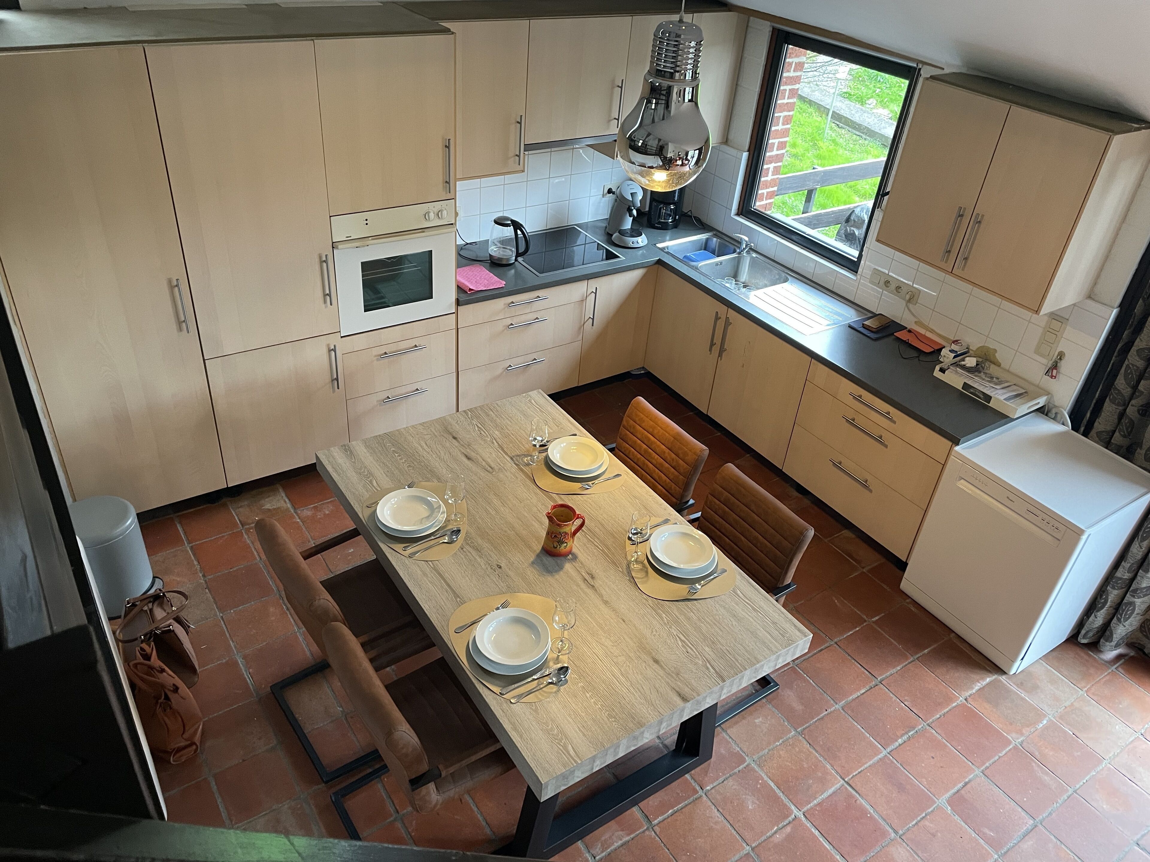 A compact kitchen with a dining table set for four, equipped with a coffee maker, kettle, and a microwave.