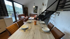 Ein Essbereich mit einem Holztisch, gedeckt für vier Personen, umgeben von Ledersesseln. Im Hintergrund ist eine Treppe zu einer oberen Ebene zu sehen.