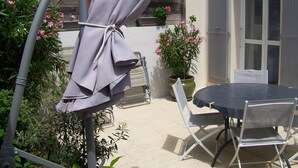 Une terrasse extérieure avec une table ronde et des chaises, un parasol et des plantes en pot.