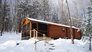 A wooden cabin with a glass door entrance, surrounded by snow-covered trees.