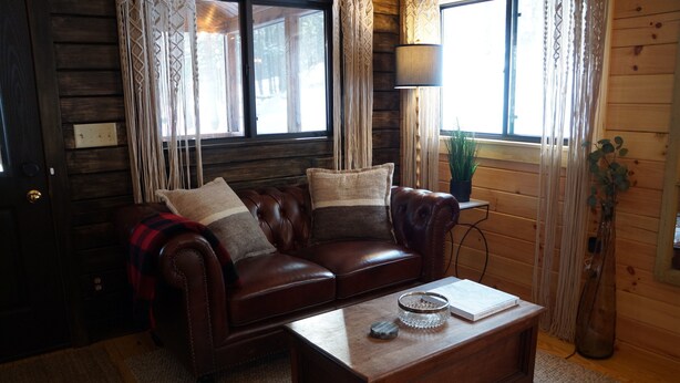A cozy living room with a leather sofa, a wooden coffee table, and a window with curtains.