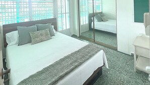 A hotel room with a large bed, a ceiling fan, a mirror, and a view of the outside through the windows.