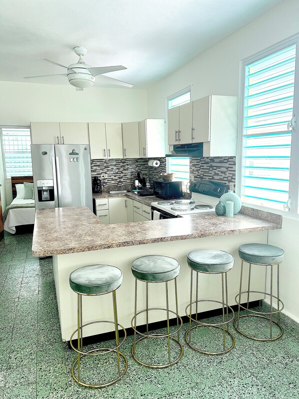 A modern kitchen with a granite countertop, stainless steel appliances, and a bar area with stools.