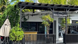 A coffee shop named Dulcesalado with a modern design, featuring a pergola, outdoor seating, and greenery.