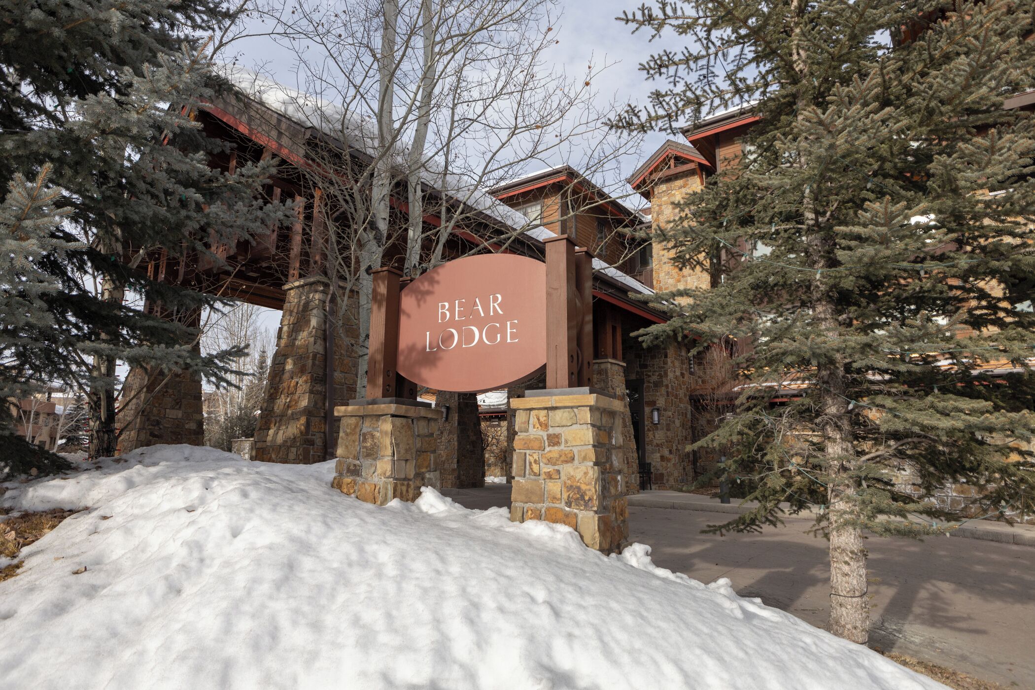 A snow-covered entrance to Bear Lodge with stone pillars and a wooden bridge overhead.
