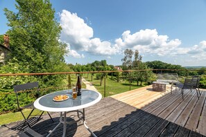 A wooden deck with a round table and chairs, a bottle of beer, and a plate of food. - Gîte Adèle - Adults only (Ajat)