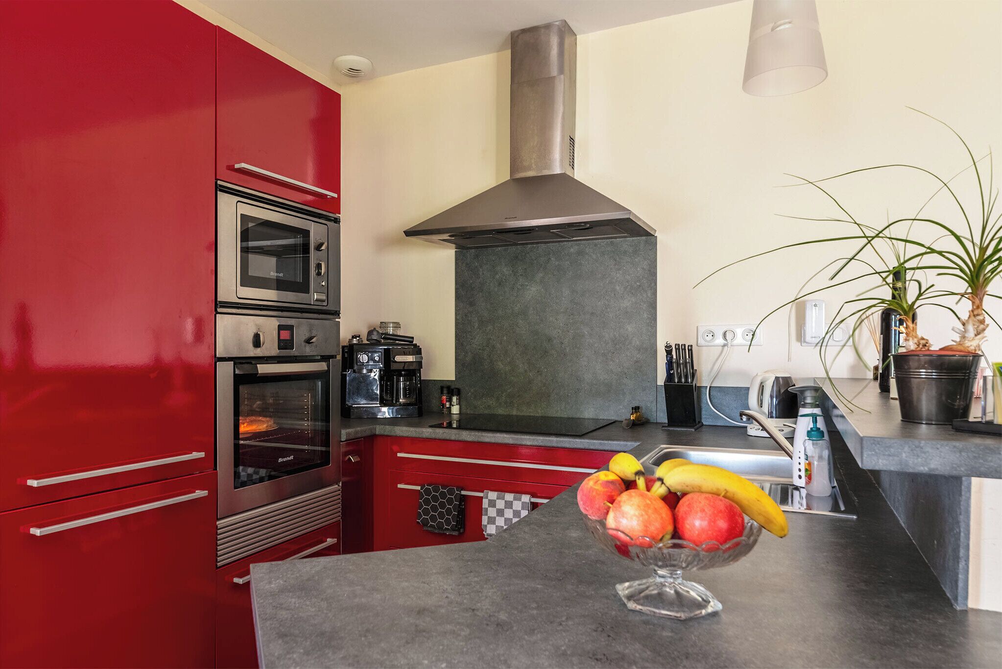Una cocina con armarios rojos, electrodomésticos de acero inoxidable y un frutero sobre la encimera.