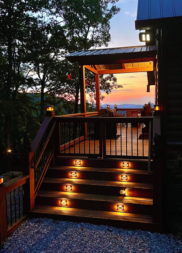 A wooden deck with steps leading to a covered area, surrounded by trees and a view of the sky.