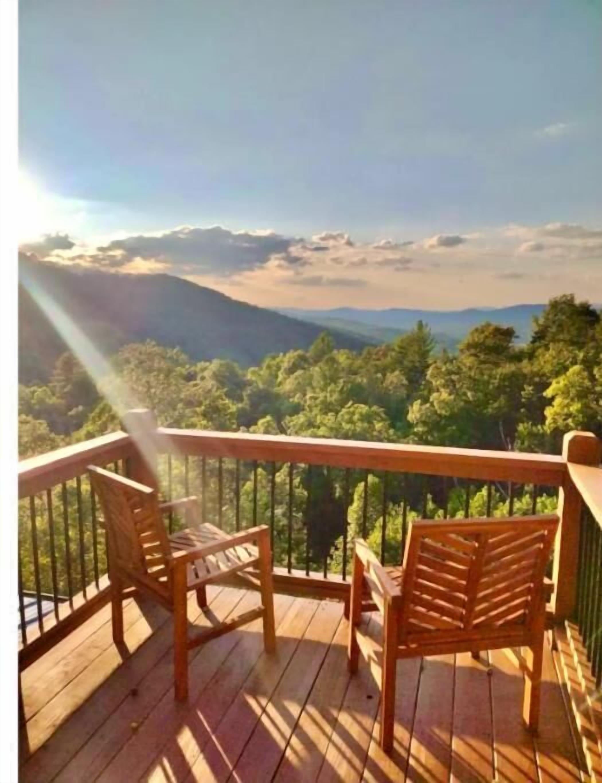 Eine Holzterrasse mit zwei Stühlen und einem Tisch, mit Blick auf eine gebirgige Landschaft.