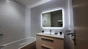 Une salle de bain moderne avec une baignoire sur pieds, un meuble-lavabo avec miroir et un revêtement mural texturé.