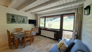 Een gezellige kamer met een eettafel, stoelen, een bank en een groot raam met uitzicht op het landschap.