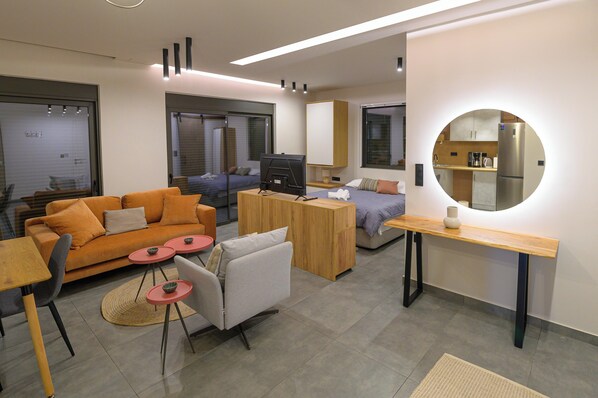 Una sala de estar moderna con un sofá, una mesa de centro y un televisor. Se observa también una zona de cocina con un refrigerador y una mesa de comedor.