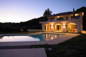 Ein modernes, zweistöckiges Haus mit Swimmingpool, Sitzgelegenheiten im Freien und einem Balkon mit Blick auf den Pool.