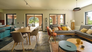 Un salon moderne comprenant un coin repas, un revêtement de sol en pierre et de grandes fenêtres offrant une vue sur l’extérieur.