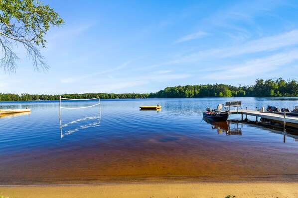 Un lac paisible, avec un quai, un petit bateau et un ciel dégagé.