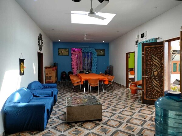 A living room with a sofa set, a dining table with chairs, a water dispenser, and a decorative wall.