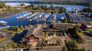 An aerial view of a marina with boats docked, a parking lot, and buildings with a red roof and a large garage.