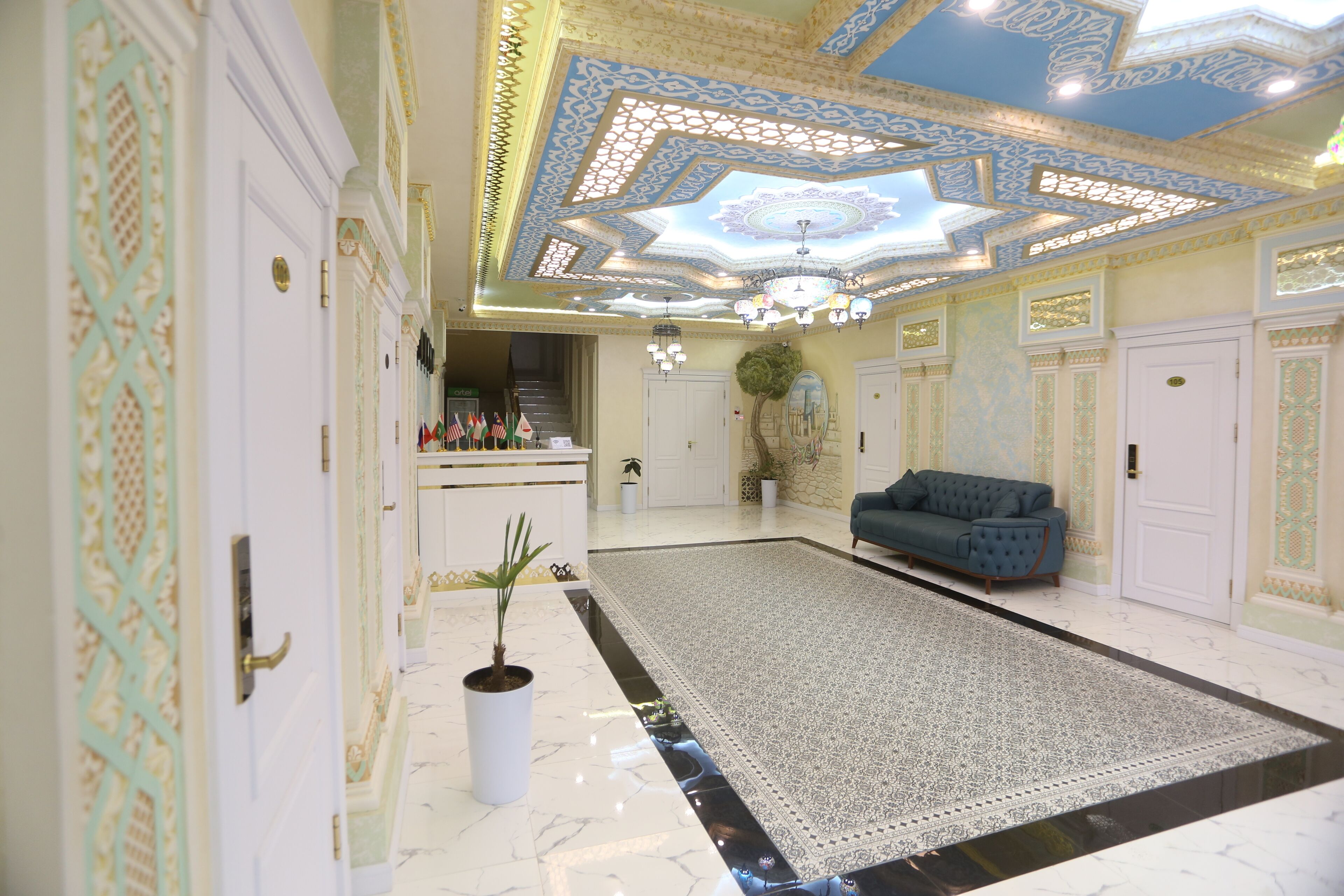 Um hall amplo com um tapete grande estampado, um sofá azul e detalhes decorativos no teto.