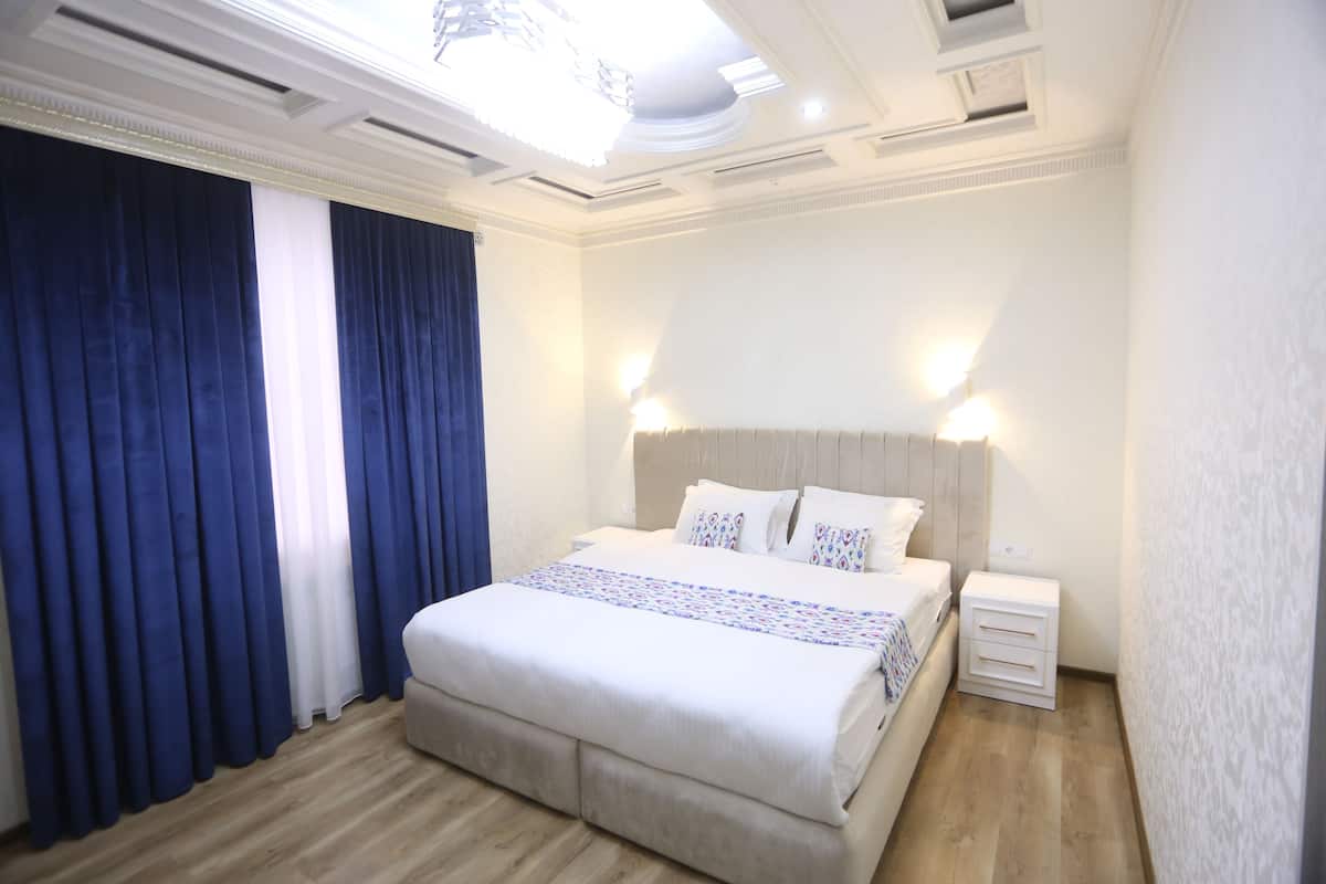 A bedroom with a large bed, white bedding, a nightstand, and a wall-mounted light.