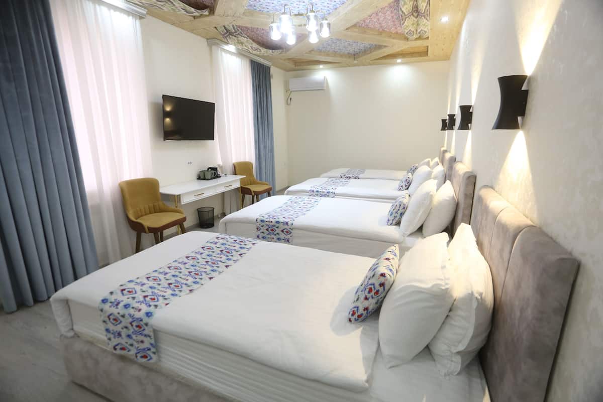 A hotel room with three beds, a desk, a chair, and a TV.