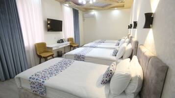 Habitación de hotel con tres camas, un escritorio, una silla y un televisor.