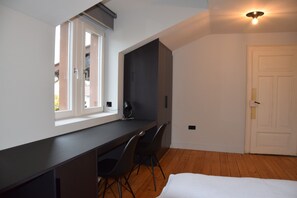 Ein Schlafzimmer mit einem Bett, einem Schreibtisch, zwei Stühlen, einem Fenster und einer Tür.