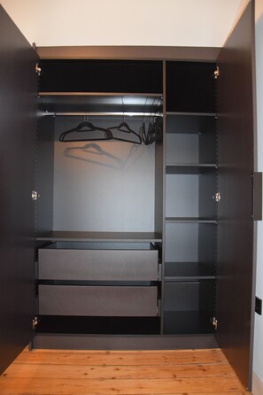 Ein begehbarer Kleiderschrank mit offenen Regalen, einer Kleiderstange und Holzboden.