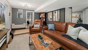 Una sala de estar moderna con un sofá de cuero marrón, una mesa de centro de madera y un sillón gris.