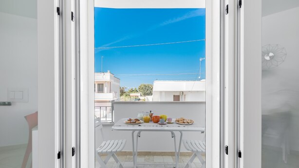A balcony with a table set for breakfast, white chairs, and a view of neighboring buildings. - 3852 Dolly House - Primo Piano by Barbarhouse (Porto Cesareo)