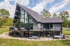 A modern house with a large glass facade, a deck, and a stone foundation.