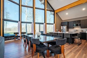 A modern kitchen with a large island, wooden flooring, and large windows.