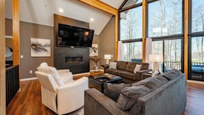 Ein modernes Wohnzimmer mit Kamin, großen Fenstern und einem Flachbildfernseher.
