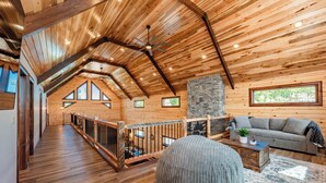 Ein geräumiger Loftraum mit Holzböden, einer Wand aus Naturstein, einem grauen Sofa, einem Holztisch und einem großen, runden Sitzsack.