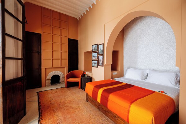 A bedroom with a large bed, a fireplace, a wooden wardrobe, and a small table with a vase.