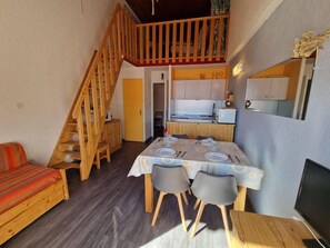 Um quarto acolhedor com escada de madeira, uma mesa de jantar posta para quatro pessoas e uma TV sobre um suporte de madeira.