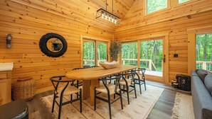 A wooden cabin interior with a large dining table, chairs, a sofa, and a fireplace. - New! Chic Chalet w/ Outdoor Fireplace & Hot Tub (McHenry)