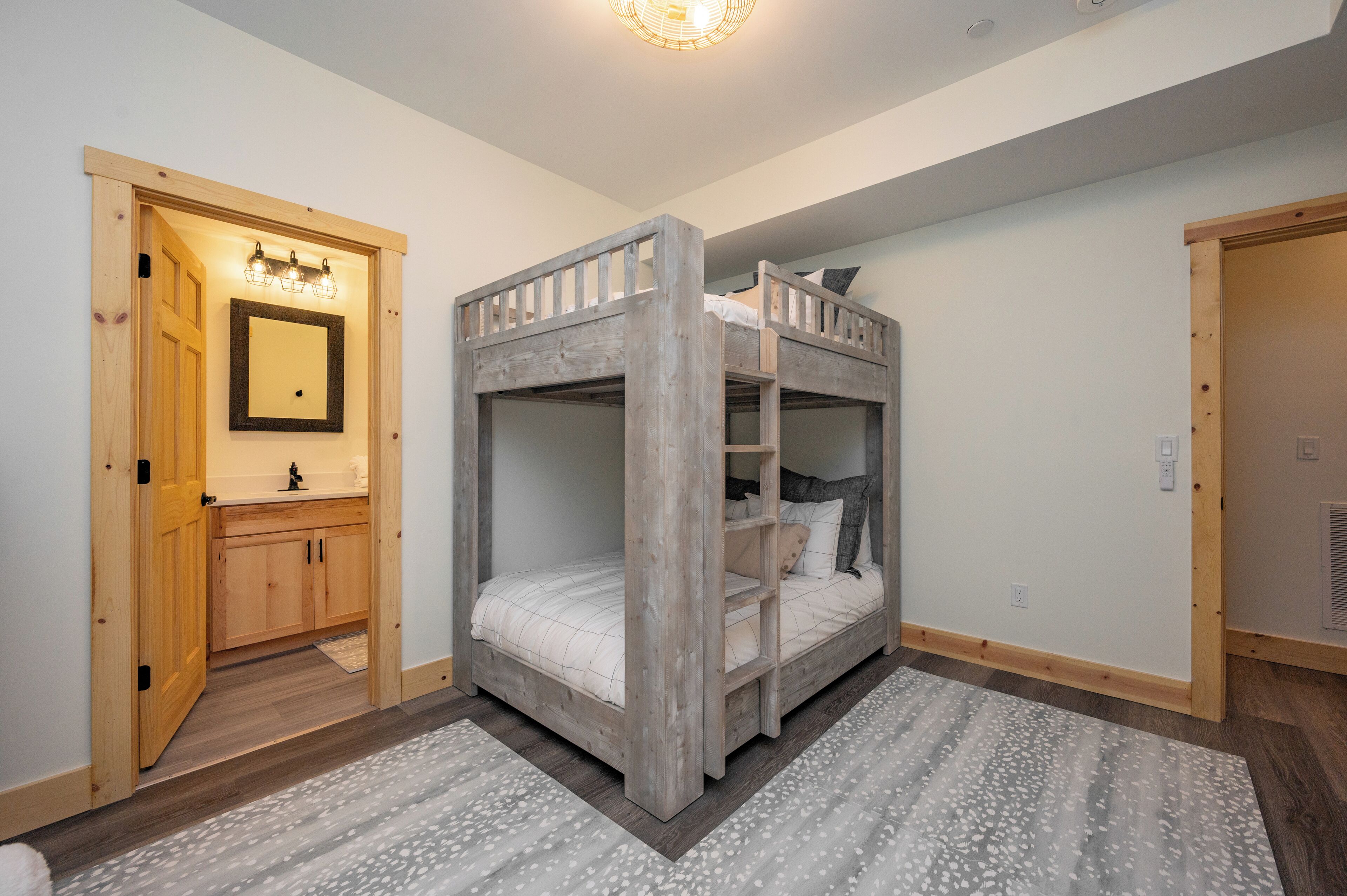 A bunk bed room with a wooden frame, a small bathroom with a mirror and sink, and a patterned rug on the floor.