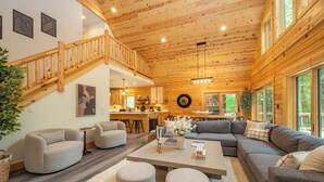 A spacious living area with a wooden staircase, a large sofa, and a dining table. - New! Chic Chalet w/ Outdoor Fireplace & Hot Tub (McHenry)