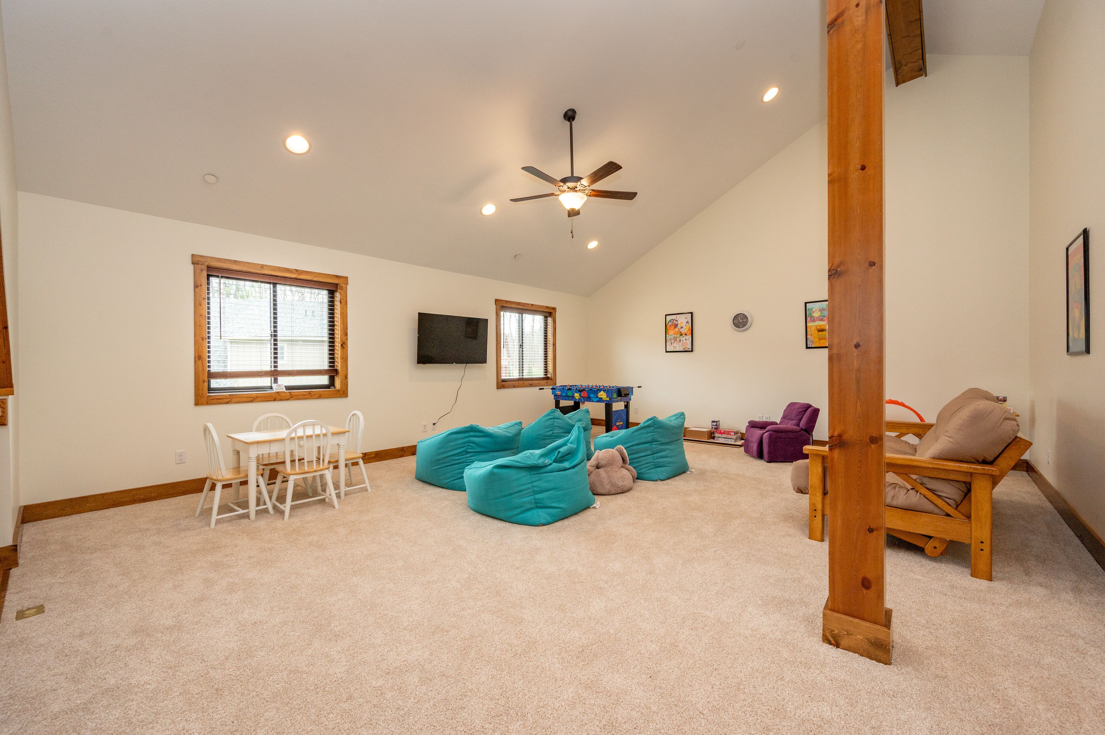 A spacious room with a ceiling fan, a dining table with chairs, and a seating area with bean bags and a wooden chair.