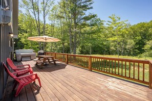 A wooden deck with red chairs, a table, and a grill.