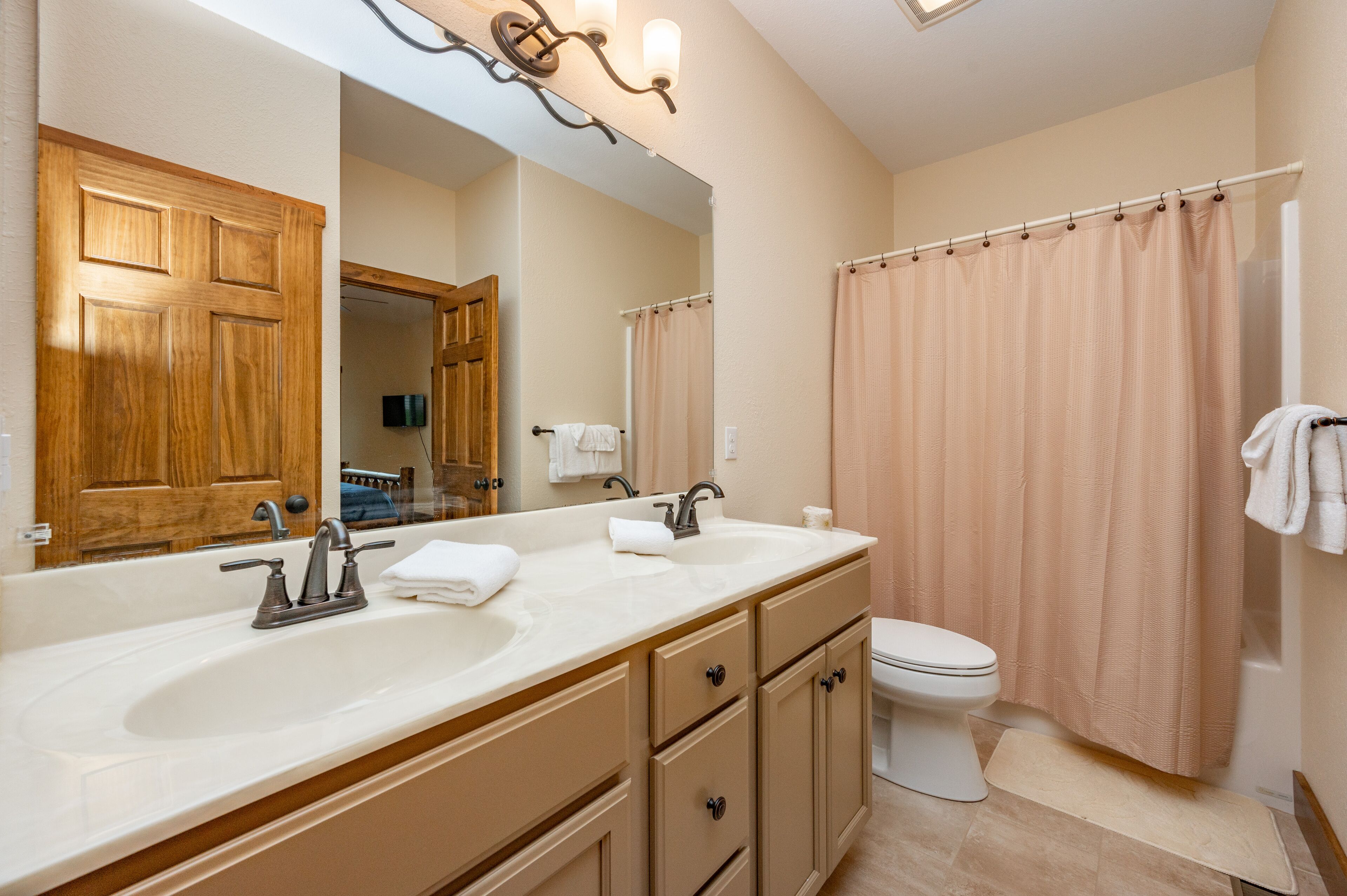 Une salle de bain avec un meuble-lavabo à deux vasques, des toilettes, un rideau de douche et un grand miroir.