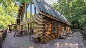 A log cabin with a deck, large windows, and outdoor seating. - Dog Friendly Lodge w/ Hot Tub & Views (McHenry)