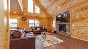 A spacious living room with a sectional sofa, a stone fireplace, and a large TV mounted on the wall.