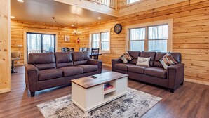 A spacious living room with two brown leather sofas, a wooden coffee table, and a large window.