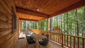 A wooden deck with a table and chairs, overlooking a forested area.