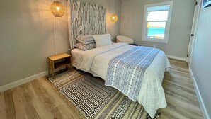 A bedroom with a bed, a nightstand, a wall-mounted light, a ceiling fan, a window with a view, and a patterned rug. - AMAZING WATERFRONT HOME WITH HOT TUB. BOTH HAVE EXTENSIVE VIEWS OF THE LAKE (Cookson)