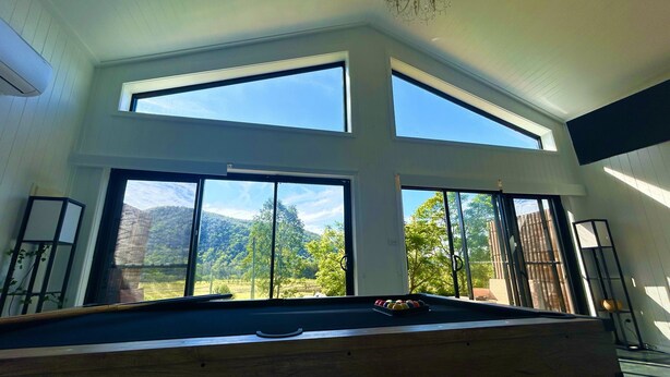 Een pooltafel met vrij uitzicht op een bergachtig landschap door grote ramen.