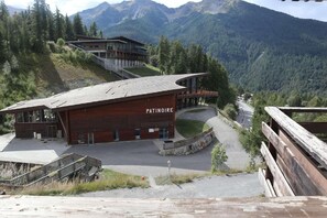 Ein großes Gebäude mit geneigtem Dach, beschriftet mit "PATINORE", inmitten einer gebirgigen Landschaft.