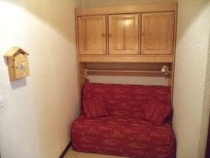 A small, enclosed space with a wooden cabinet above a red patterned sofa. - 10m from ski slopes, 3rd floor, view mountain, balcony, tv, ski locker, 28m², Les Orres (Les Orres)